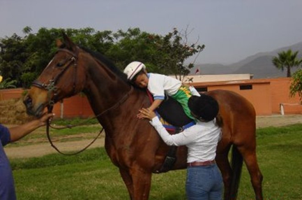 Niño montado en un caballo y abrazándolo. Se ve como una mujer cuida del niño